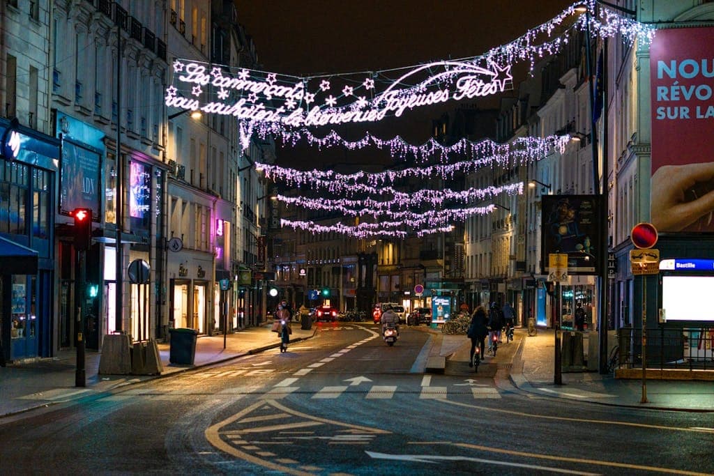 Nighttime view of a beautifully lit street in Paris, showcasing festive holiday decorations and vibrant urban ambiance.